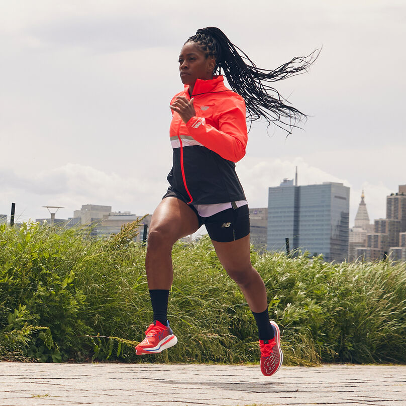 Young woman in a bright orange jacket running in the park.