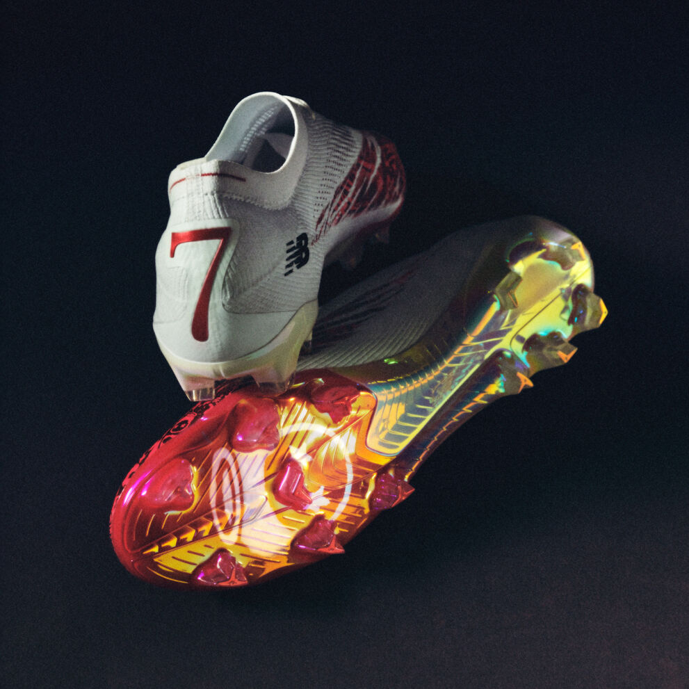 Pair of white soccer cleats with red accents and multicolor sole on a dark background.