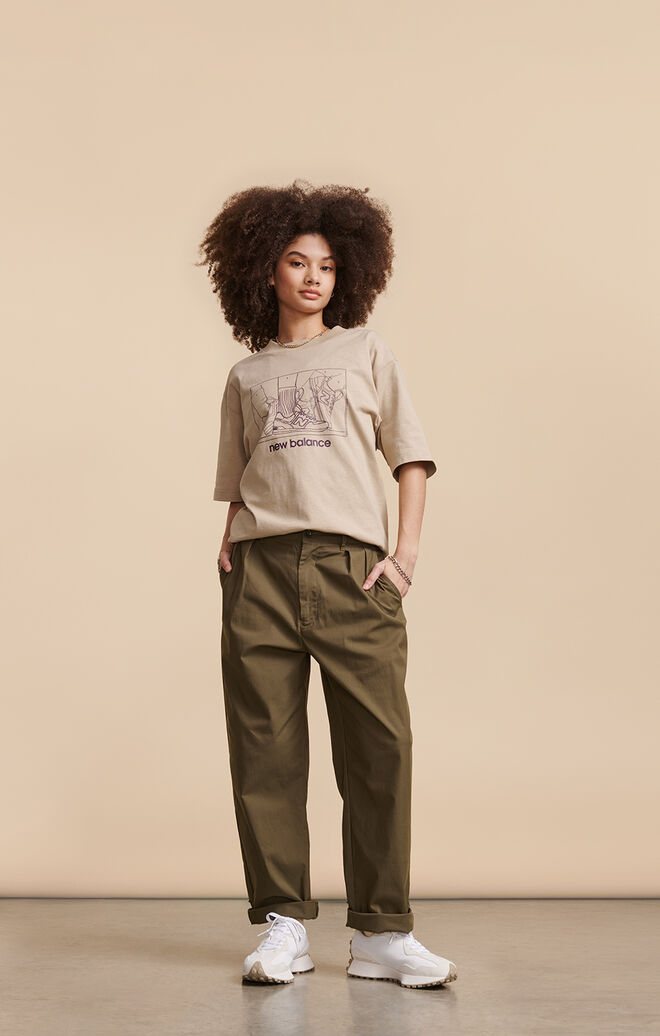 Woman wearing tan New Balance graphic t-shirt with white jacket posed against beige background in studio environment 