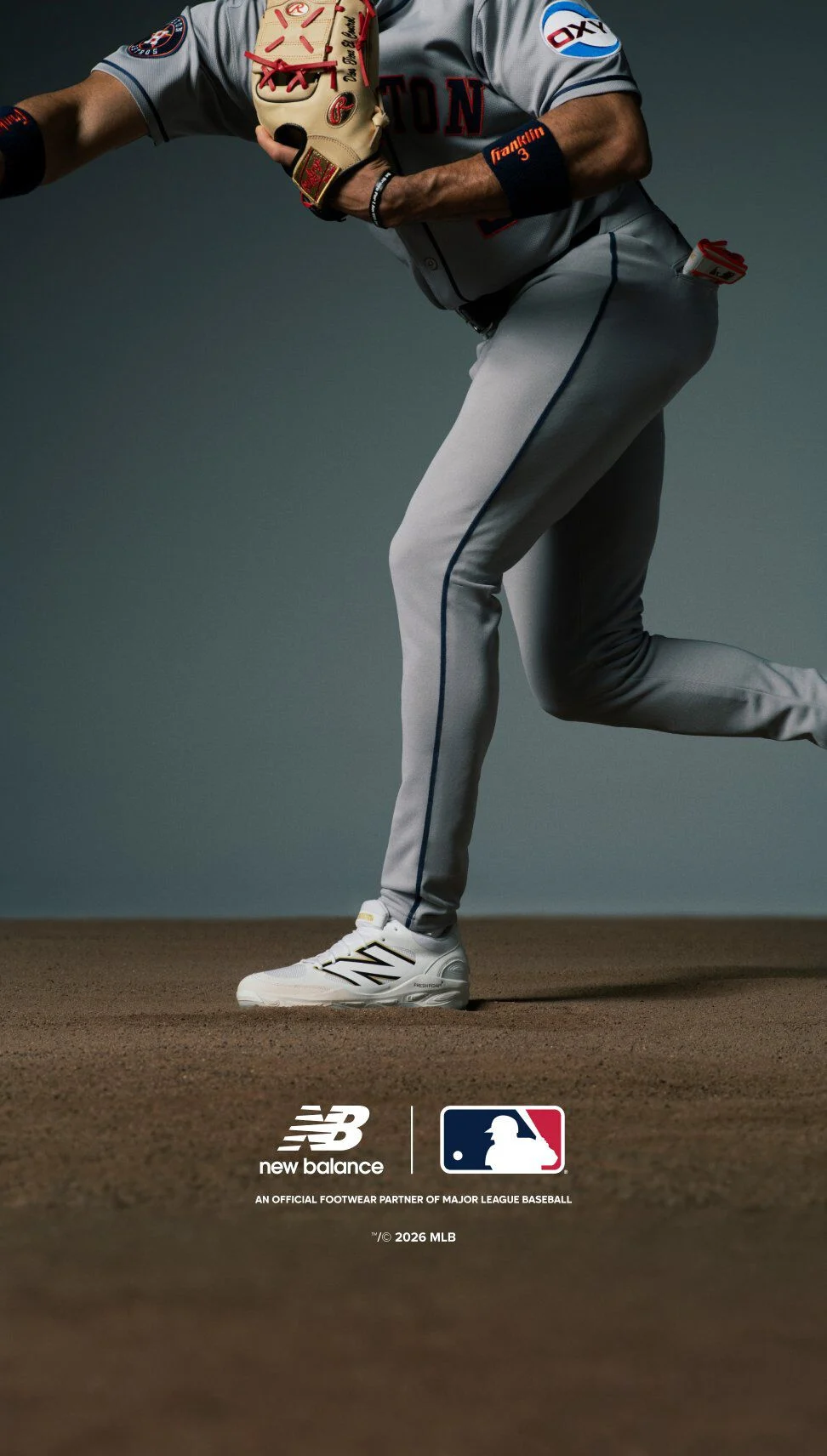 A baseball player wearing a gray uniform with navy and orange accents is positioned in a ready stance, holding a tan glove with red stitching.
