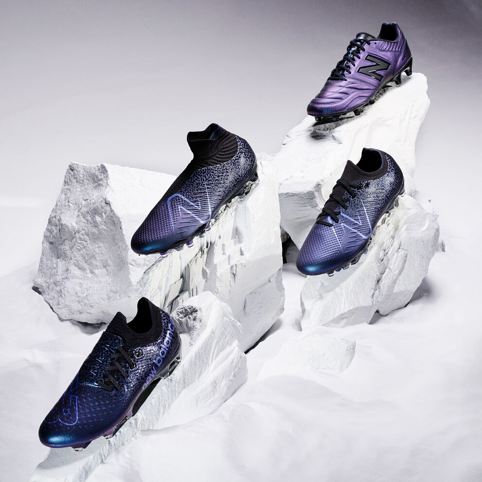 Four purple and black soccer boots sitting on top of snowy rock. 