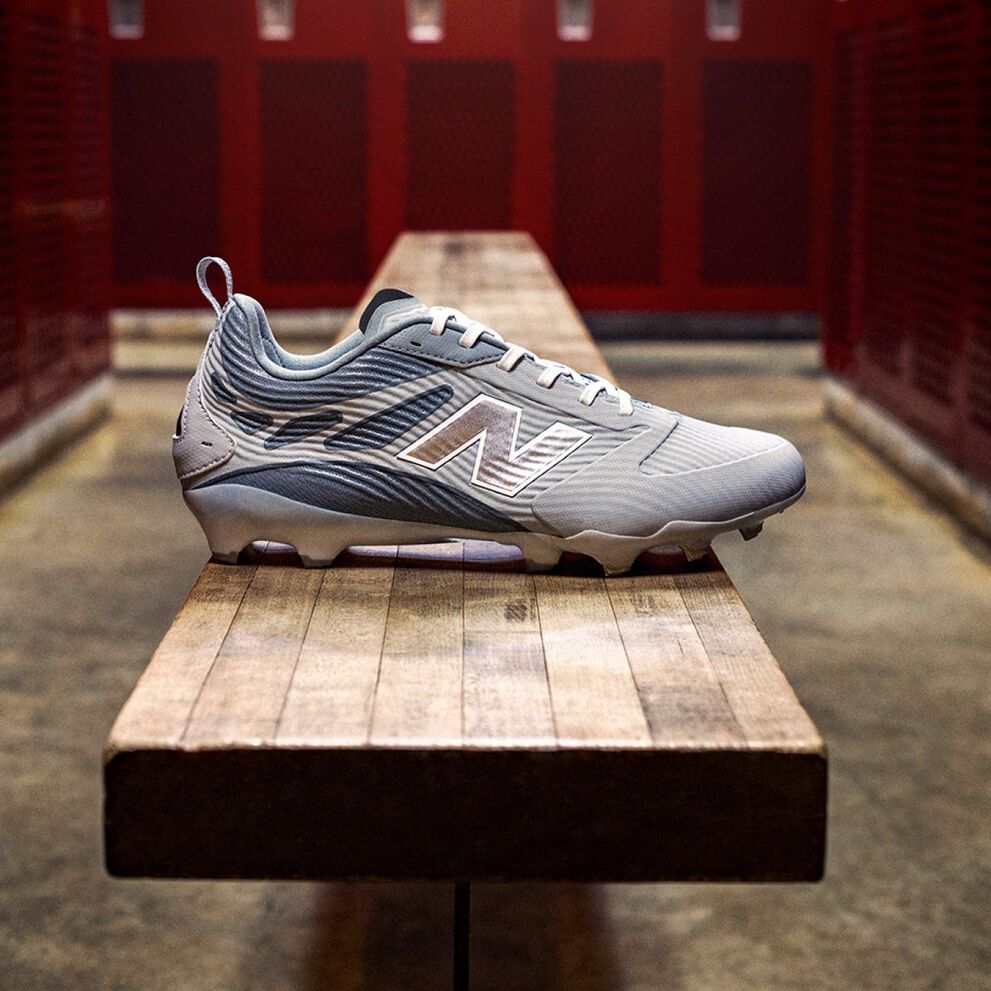 Botas deportivas New Balance gris claro apoyadas en un banco de madera del vestuario.