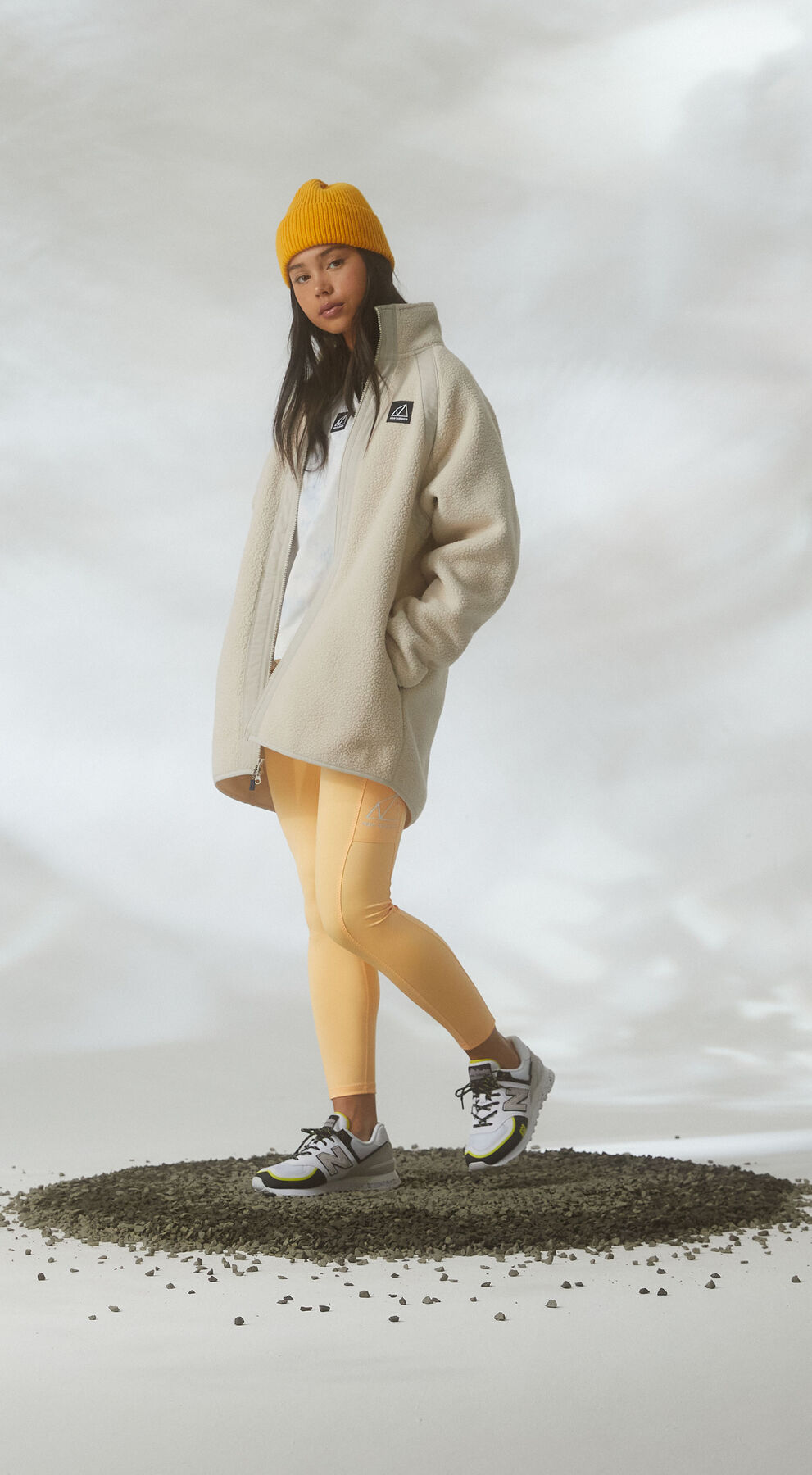 Woman standing in gravel against cloudy studio environment wearing All Terrain gear and 574 shoes