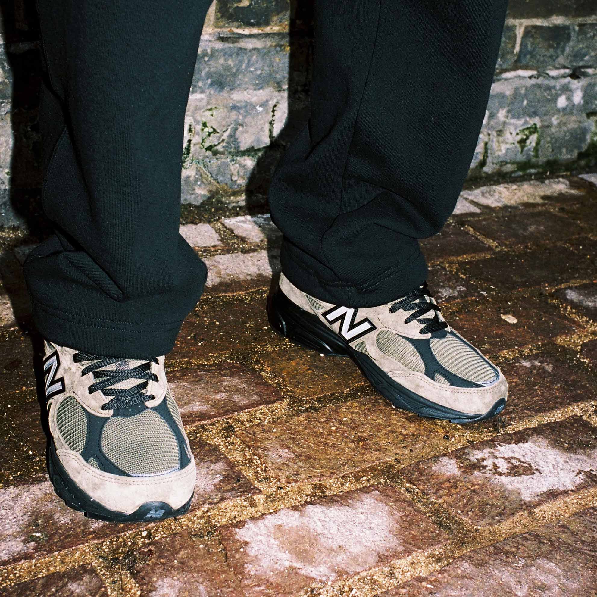 Split image, the left with a black frame around a man standing in the street wearing brown 990v3 shoes and the right, a close-up of the 990v3 shoes