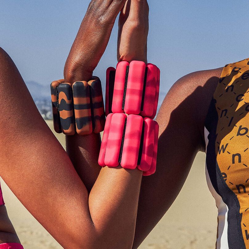 2 women locking arms wearing gold and pink Bala bangles around wrists set in desert scene with blue sky