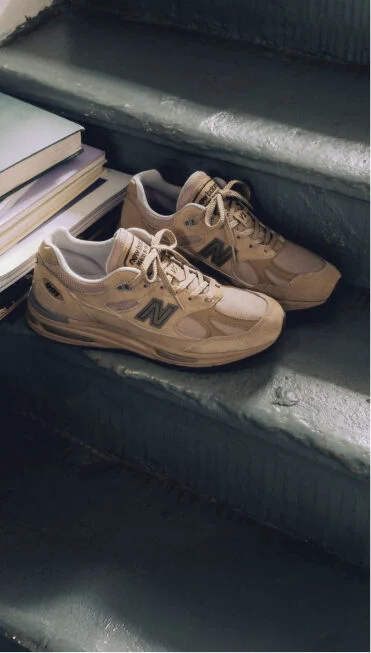 A pair of New Balance Made in UK sneakers on a staircase next to a pile of books.