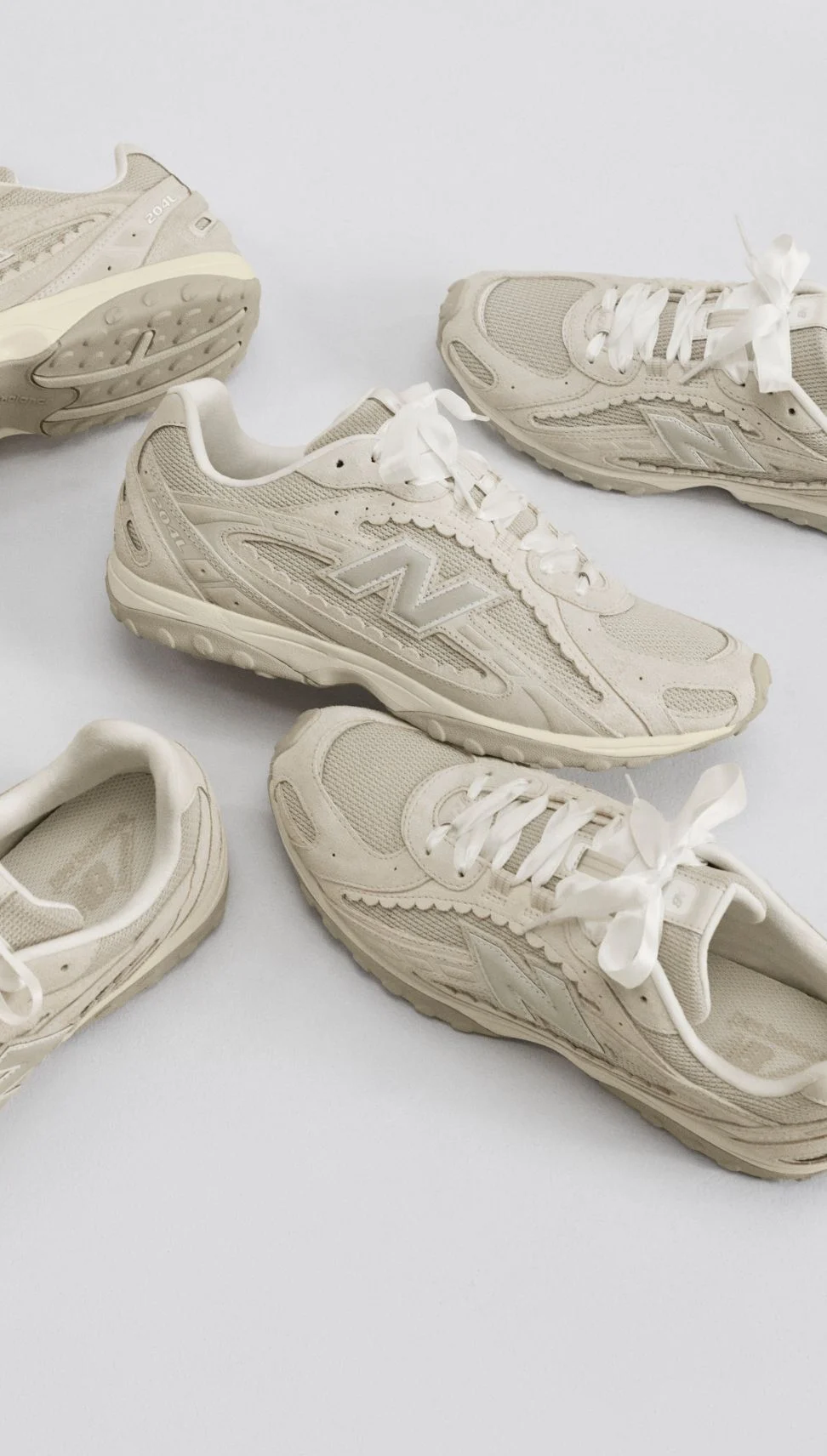 Multiple cream-colored sneakers sitting on a grey studio backdrop. 
