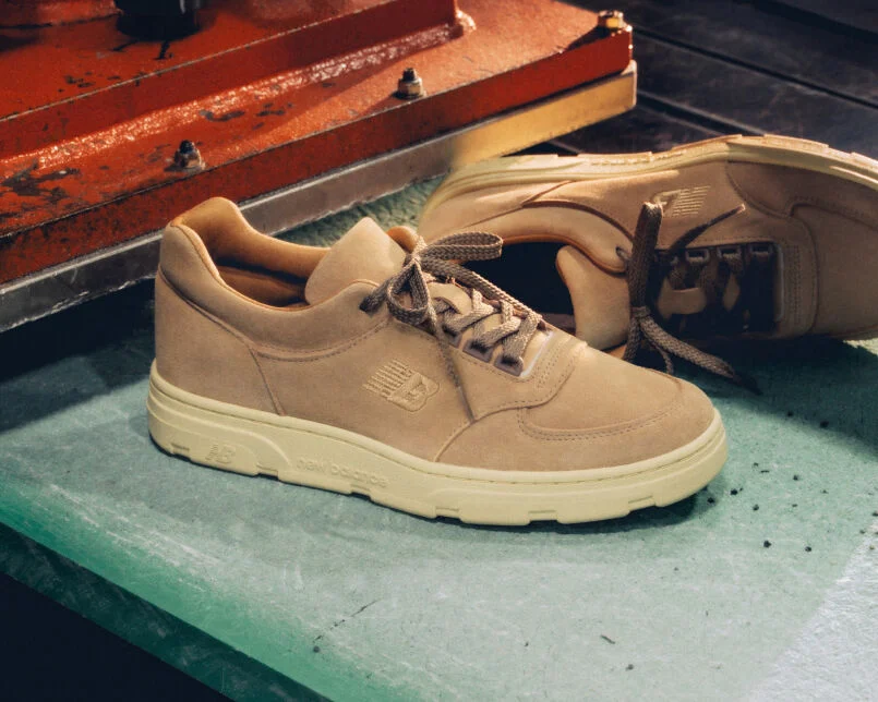 Knee down view of a woman wearing a pair of New Balance Made in UK sneakers standing in a beige studio environment.