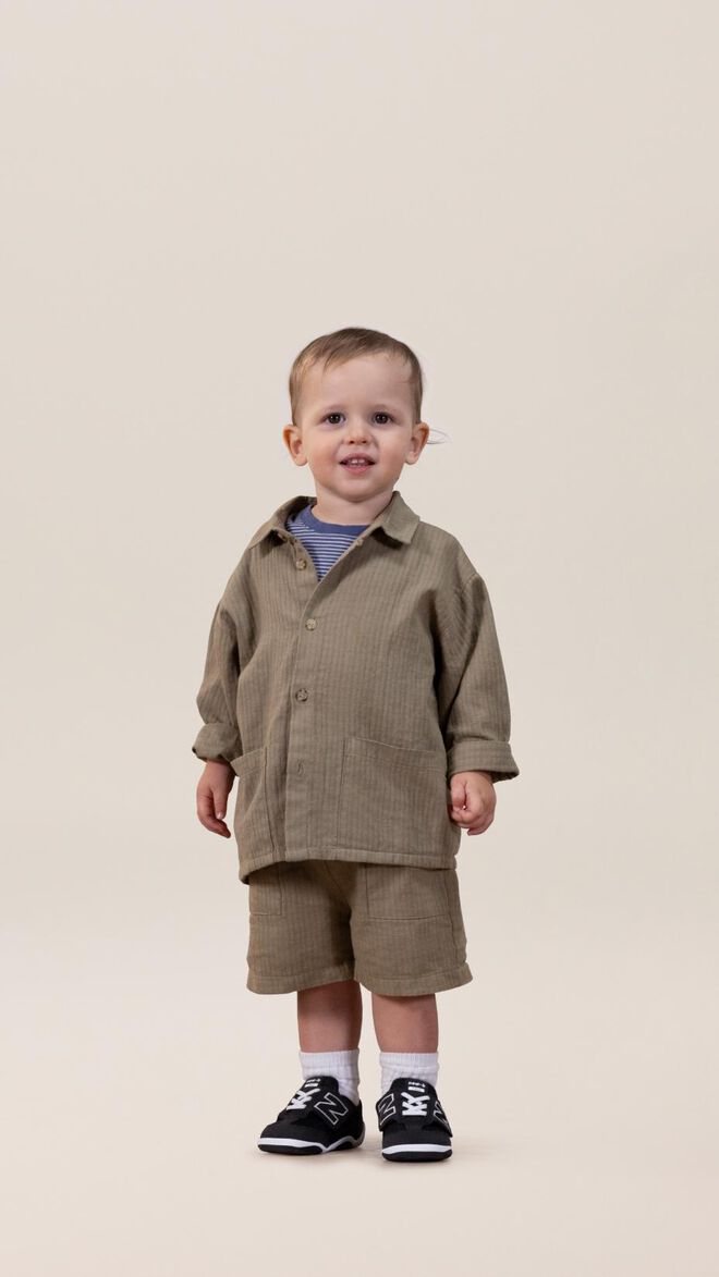 Toddler wearing an army green matching set standing in front of a beige background. 
