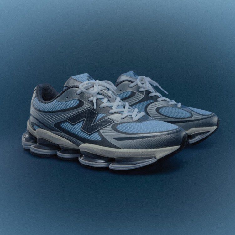 The ABZORB 2000 New Balance sneaker in an angled profile in light chrome blue and silver metallic over a blue radial gradient background. 