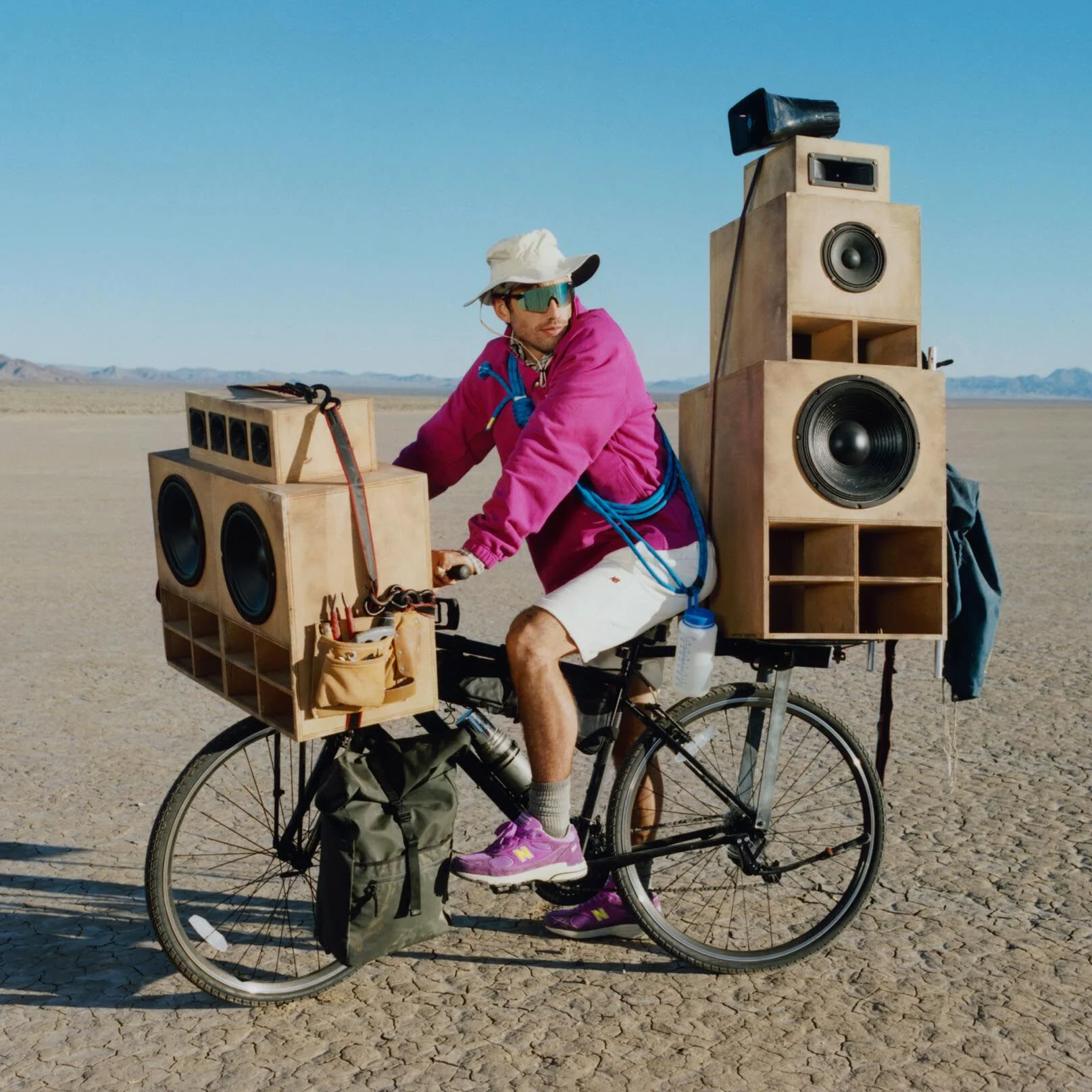 Guy on a bike with giant speakers attached to it wearing a purple sweater and shoes.