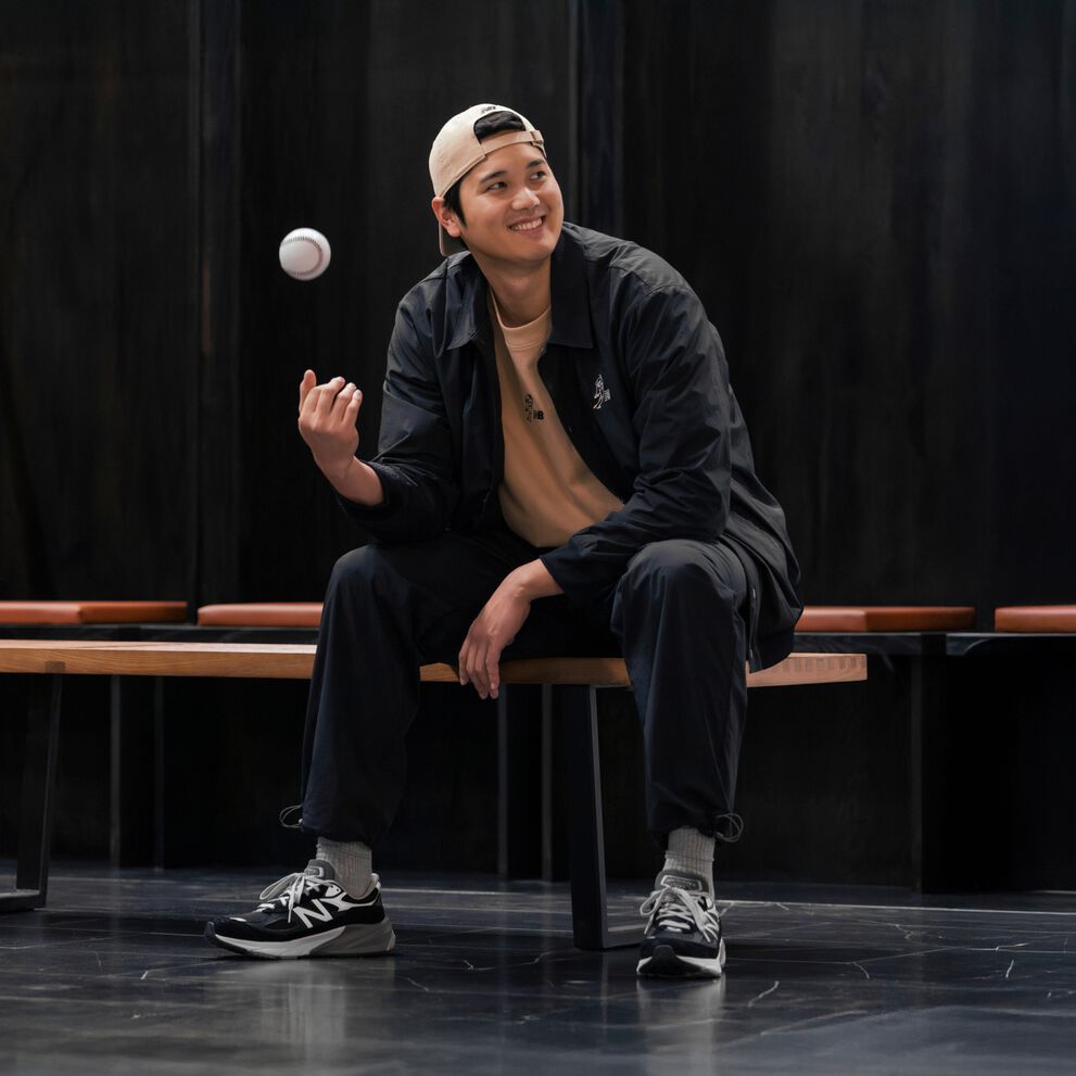 Ohtani sentado en un vestuario lanzando una pelota al aire.  