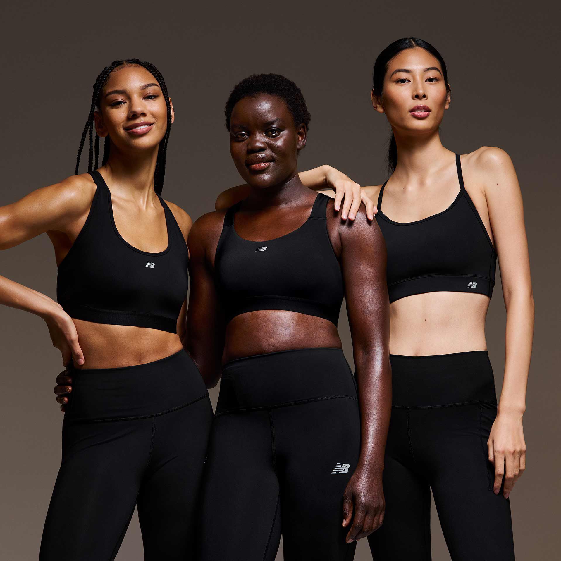 A group of women wearing sports bras and leggings in front of a dark background.