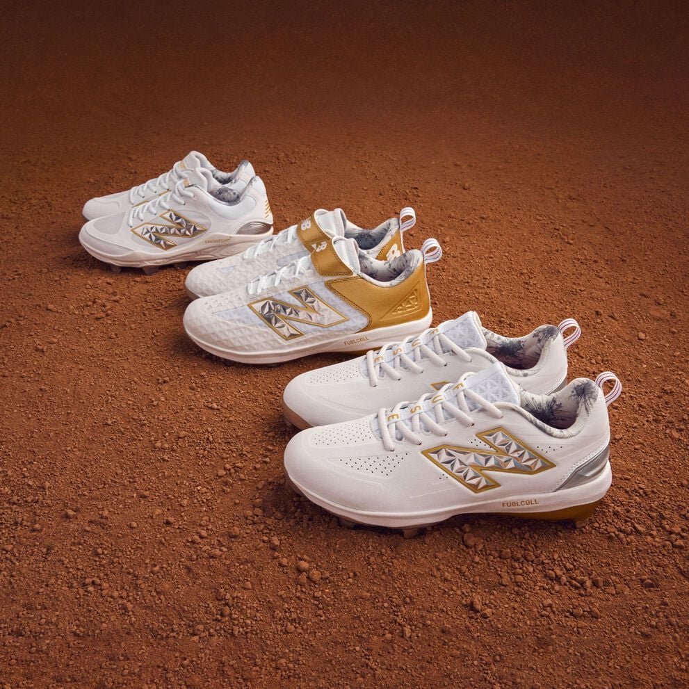 Three pair of gold and white cleats sitting on dirt.    