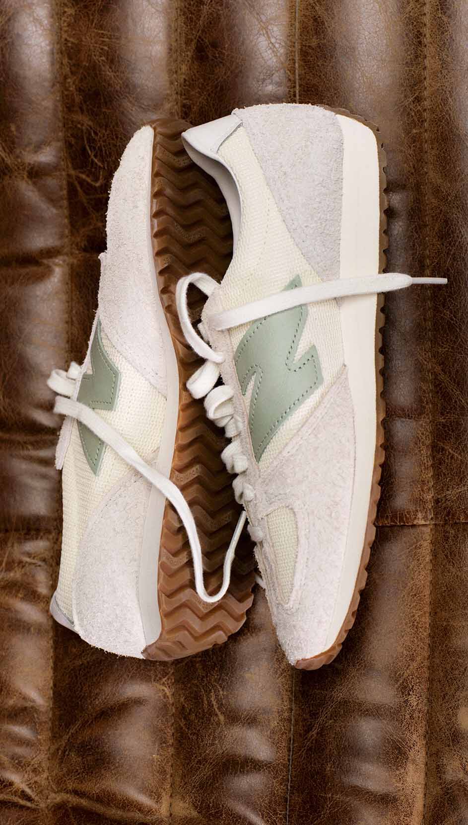 A pair of light tan colored 471 sneakers lying on a dark brown couch.