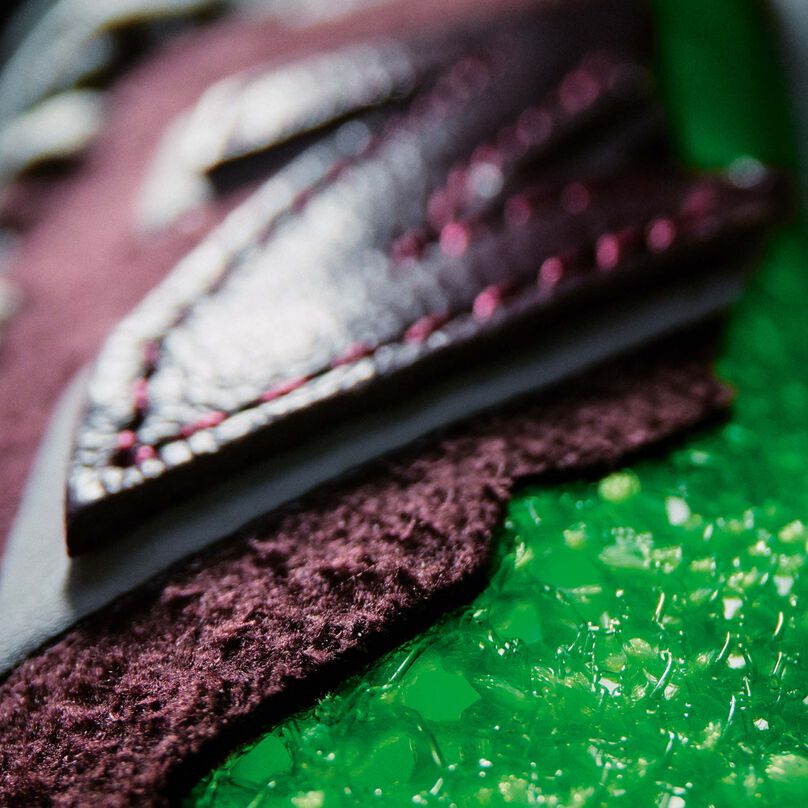 A dramatically lit detail shot of the upper textures of a NB Stone Island Tokyo Design Studio dark reddish brown FuelCell RC Elite running shoe with lime-green accents