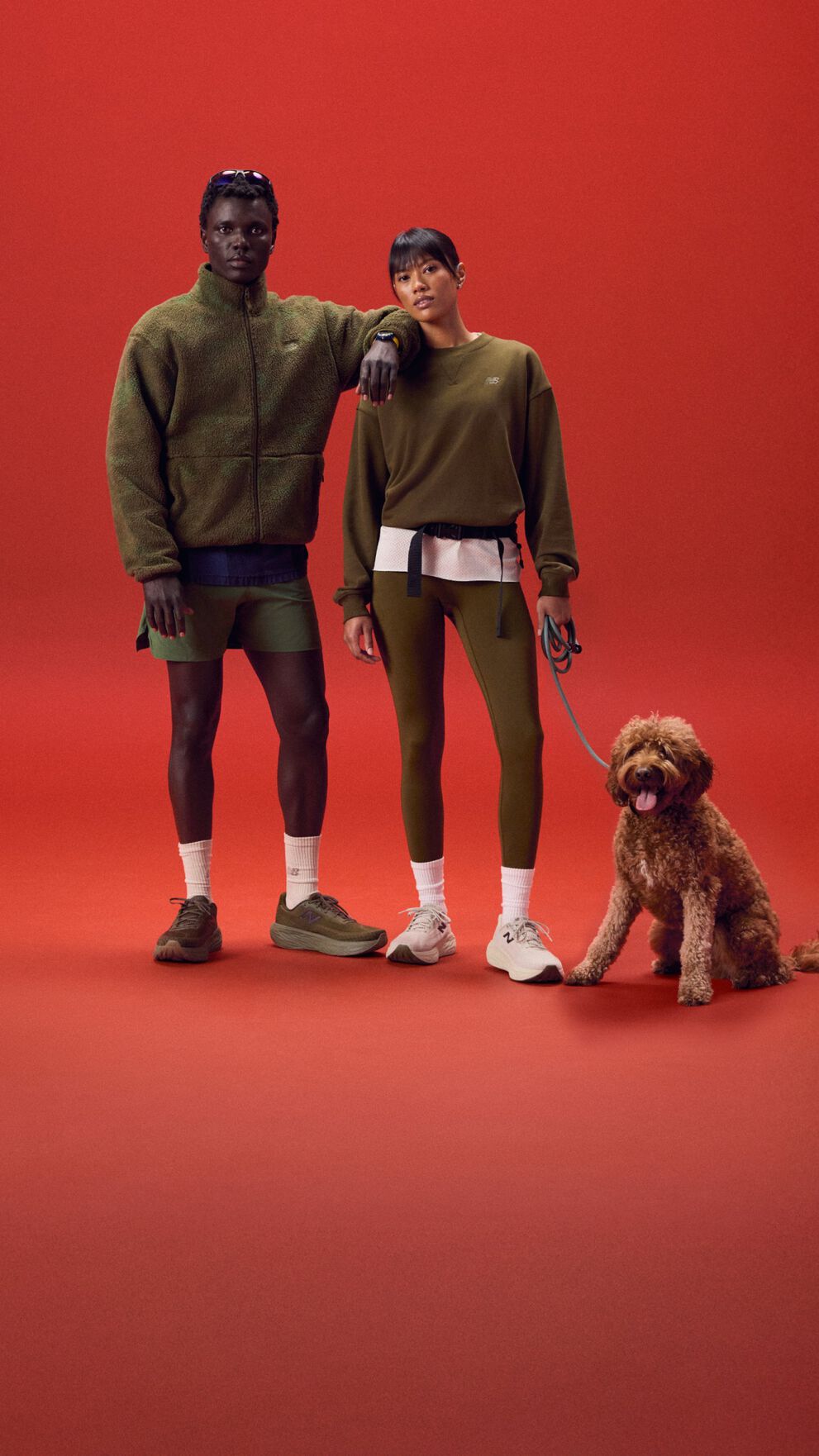 Pareja joven de pie sobre un fondo rojo con un perro.