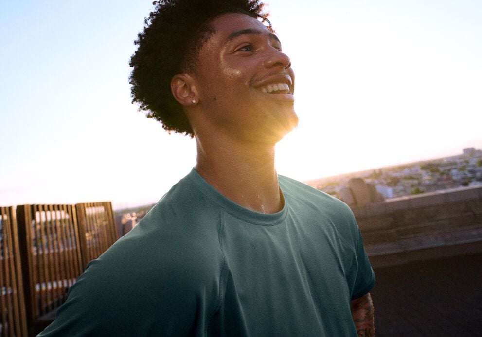 Athlete in a teal performance T-shirt standing on a rooftop training area at sunset.
