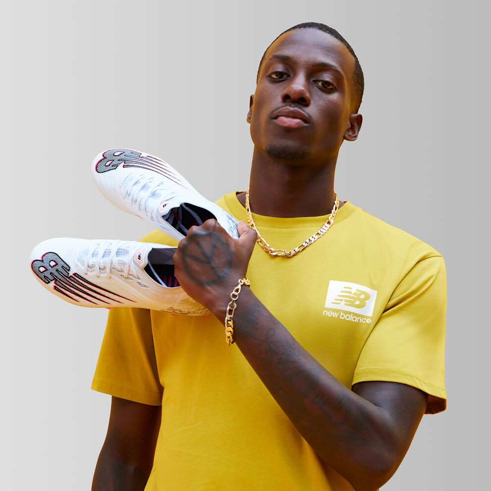 Tim wearing a yellow tshirt holding up soccer boots on a grey background.