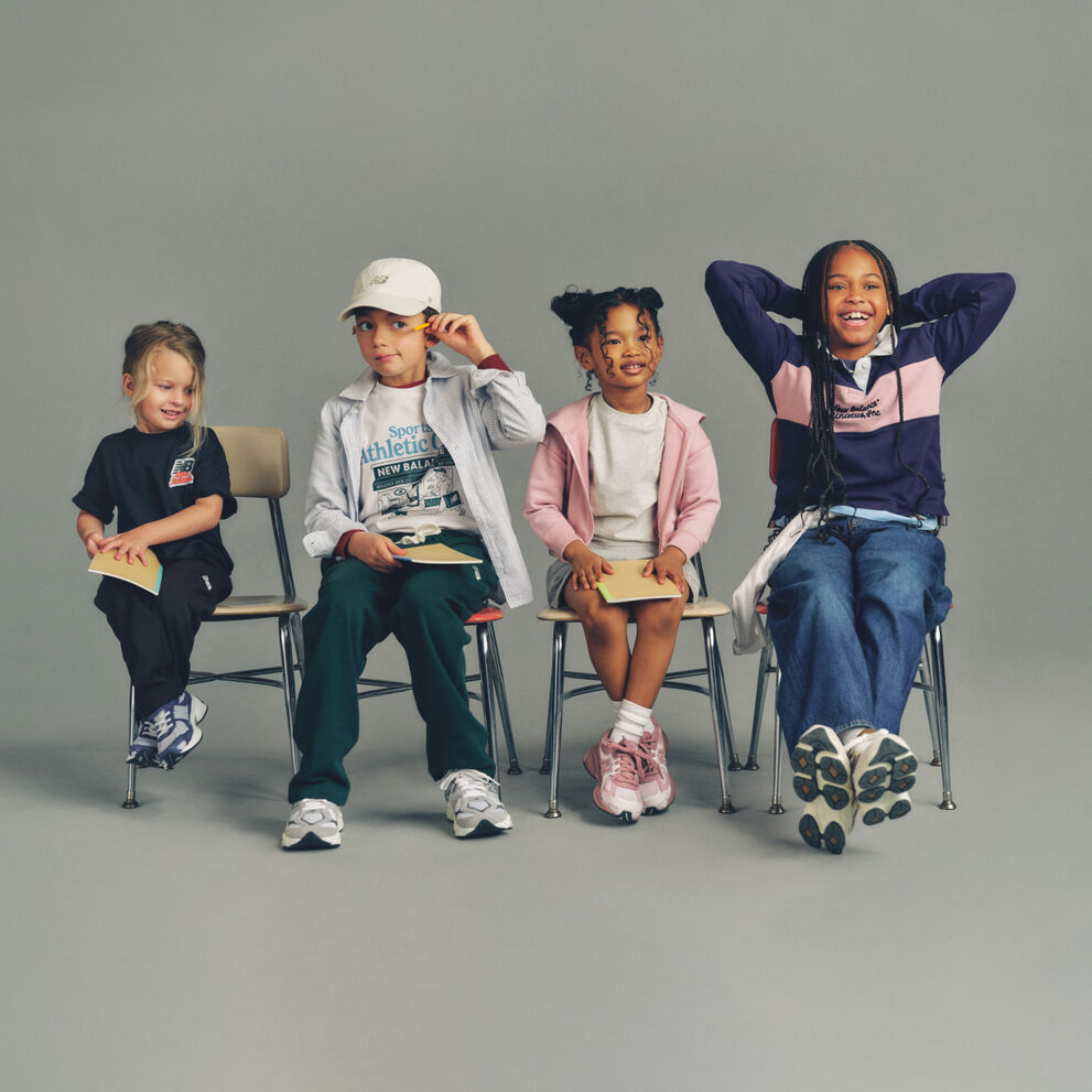 Three kids seated side-by-side on simple wooden chairs against a plain, neutral background, arranged in a horizontal line.