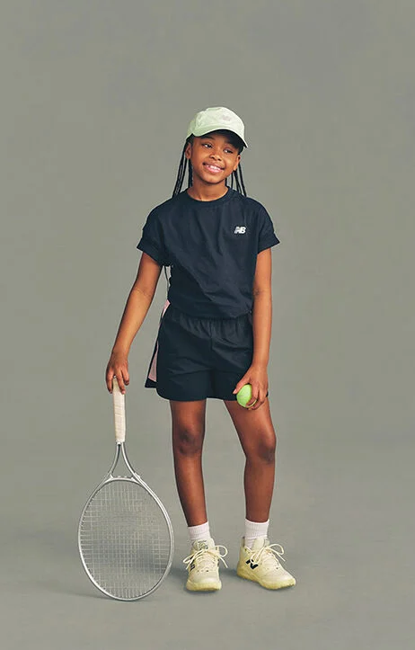 Kid holding a tennis racket against a grey studio background.