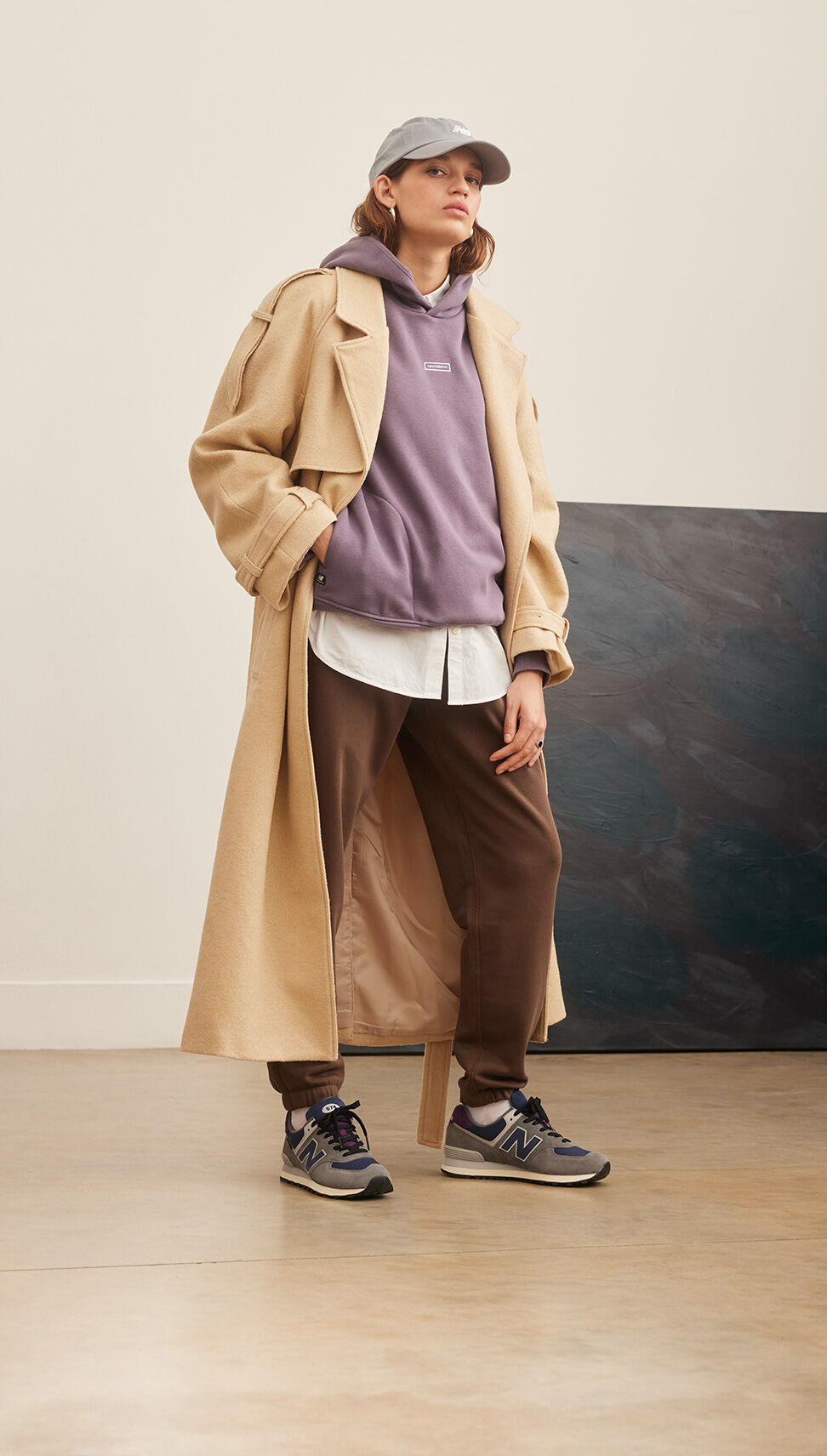 Woman wearing NB apparel, a tan trench coat and a pair of 574s 