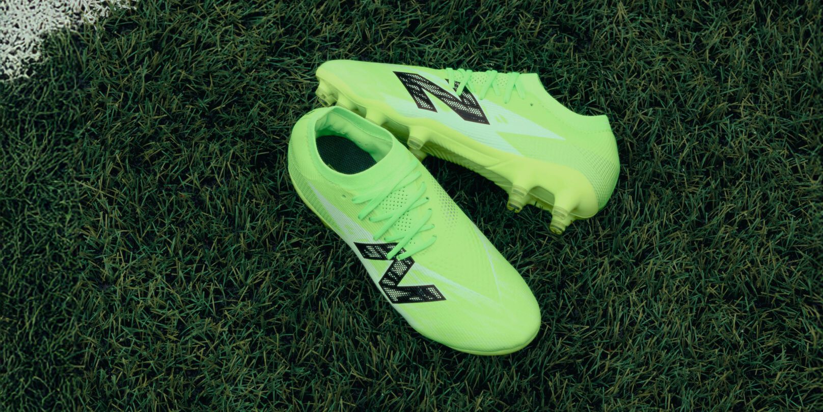 Pair of neon green cleats laying on the pitch.