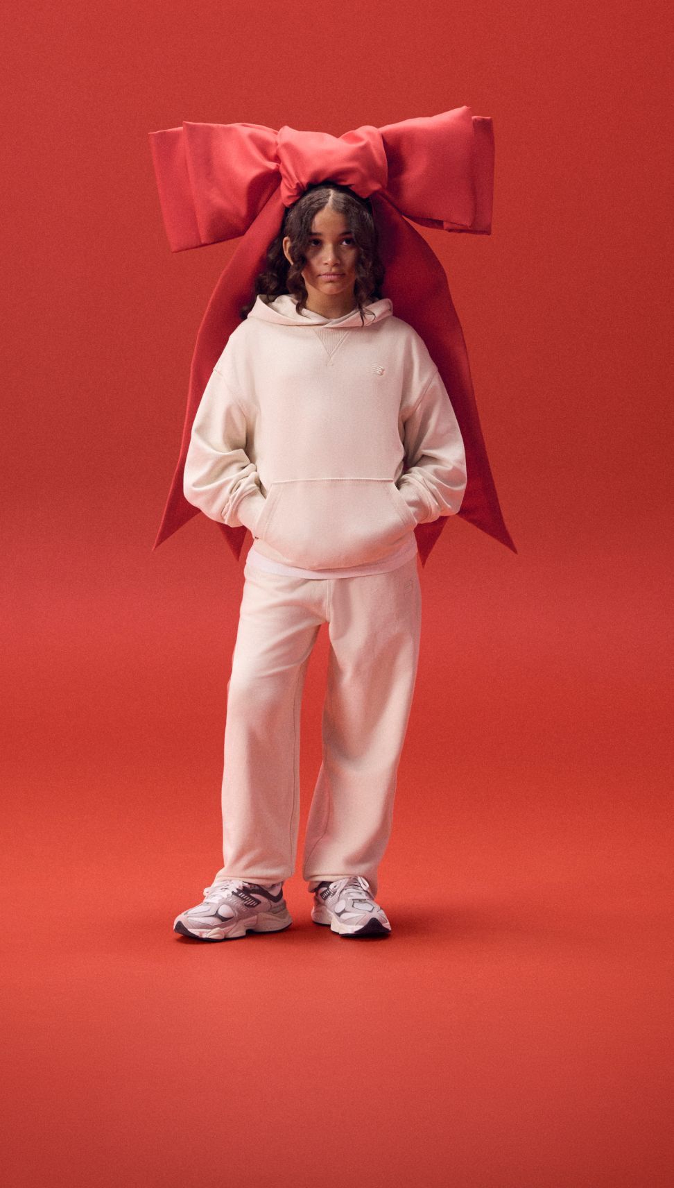 Kid wearing a large red ribbon on her head in a white outfit. 