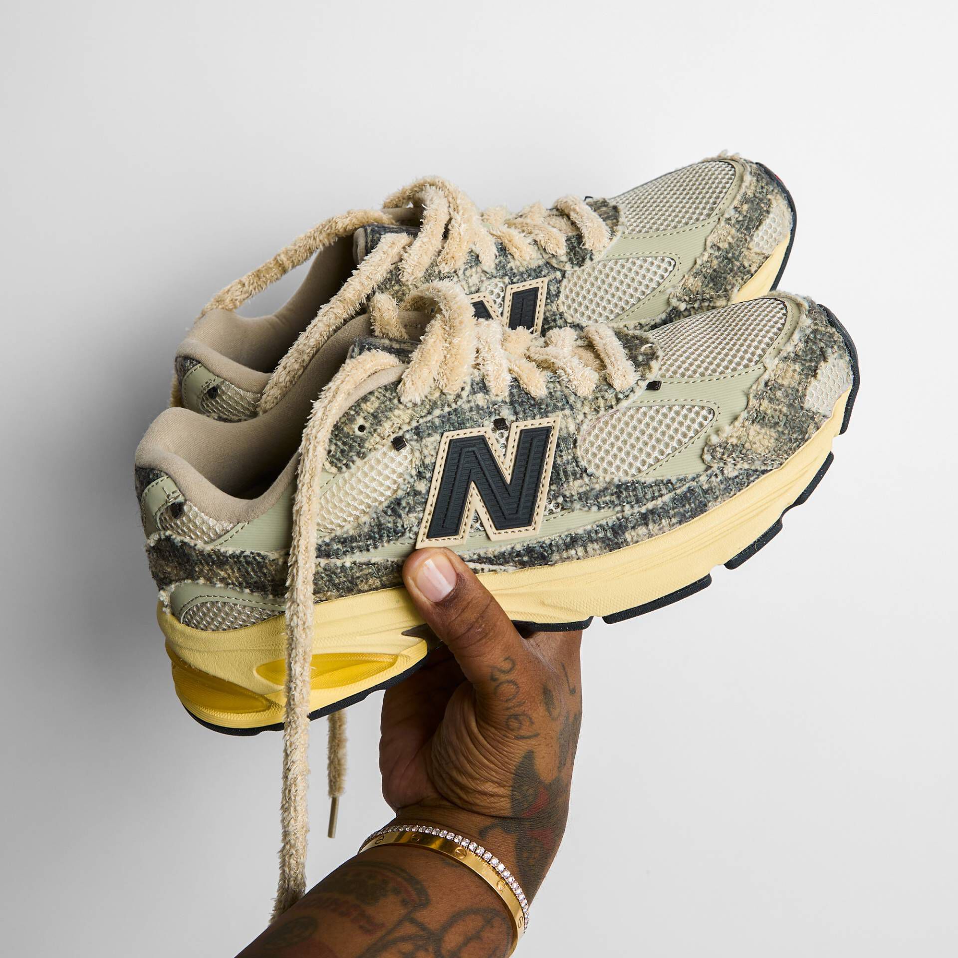  A person holding a pair of New Balance shoes against a white background.