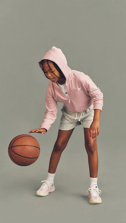 Kid playing with a basketball against a grey studio background.