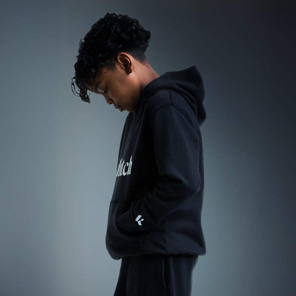 Boy wearing a black hoodie with hands in the front pocket, shown in a side profile.