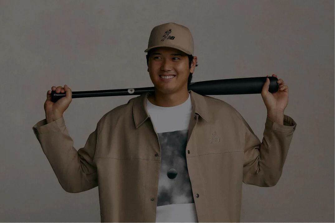 Ohtani standing and holding a baseball bat behind his head wearing a tan jacket
