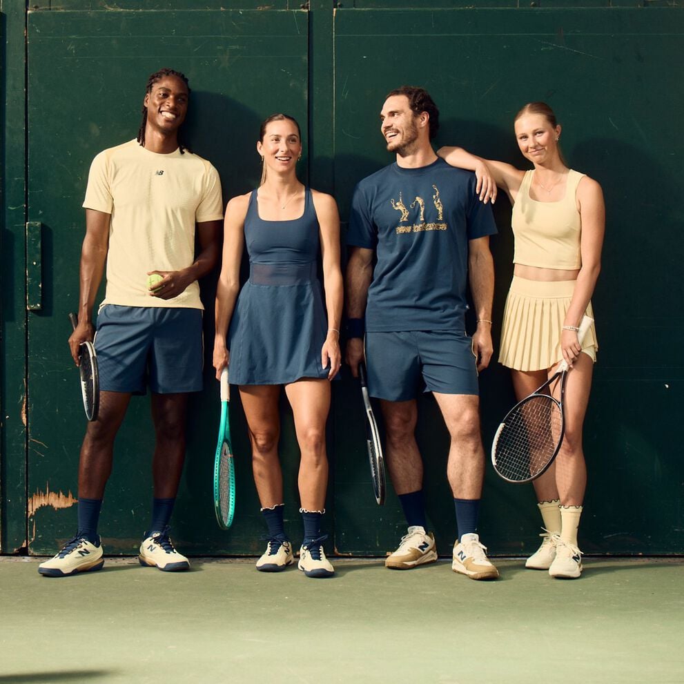 Four tennis players in coordinated athletic apparel stand against a dark green court wall holding rackets and a tennis ball.