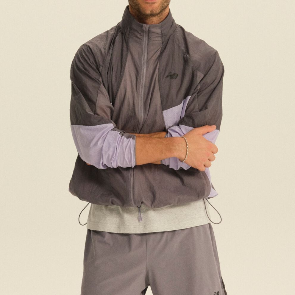 Person wearing a gray and lavender color-block performance jacket and gray athletic pants in a clean studio setting.