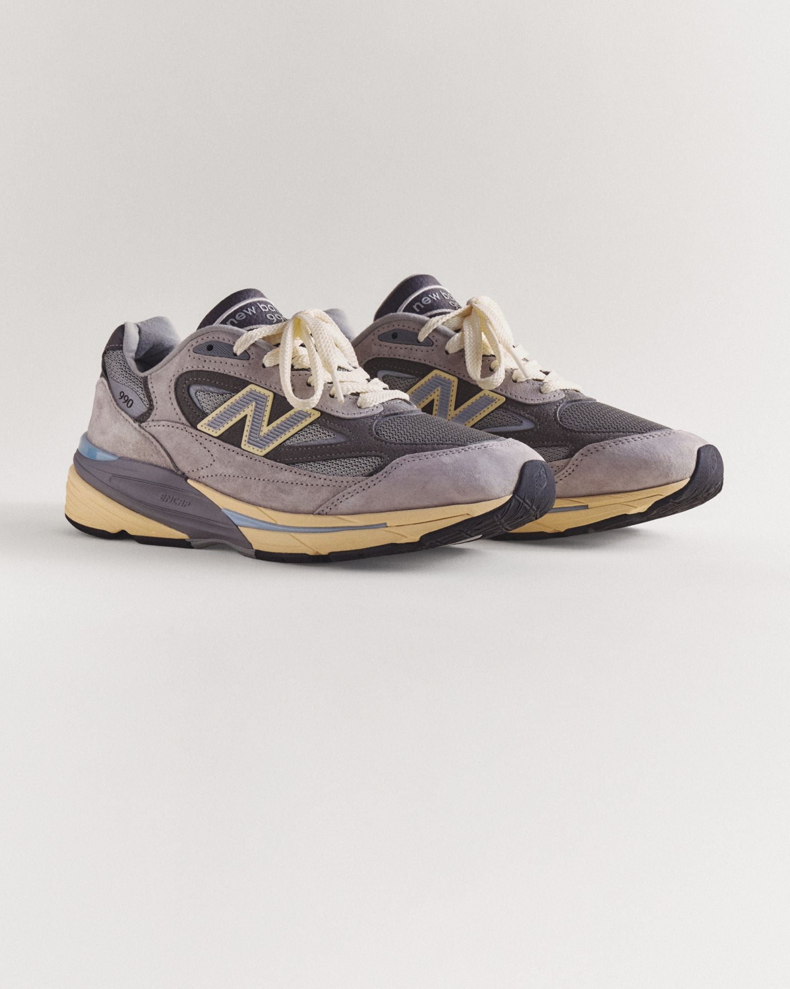 A pair of grey 990v7 sneakers sitting on a grey studio backdrop.