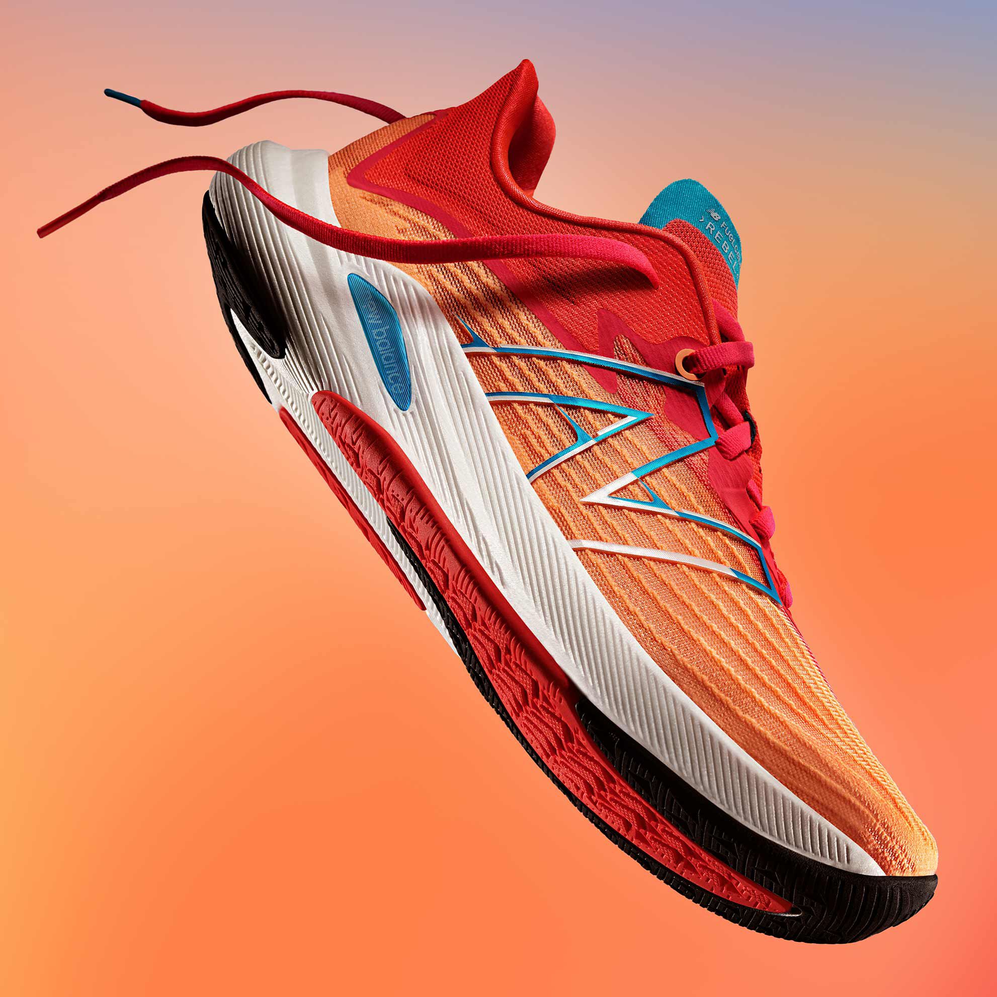 A dramatically lit women’s orange and red NB FuelCell Rebel v2 running shoe on a warm gradient background