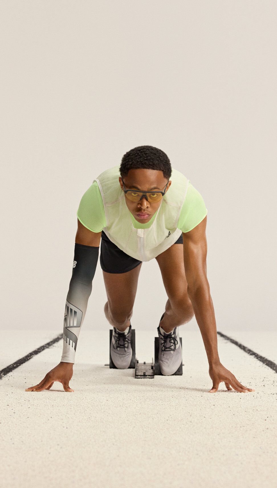Athlete in a sprint start position on a track, with hands on the ground and feet secured in starting blocks.
