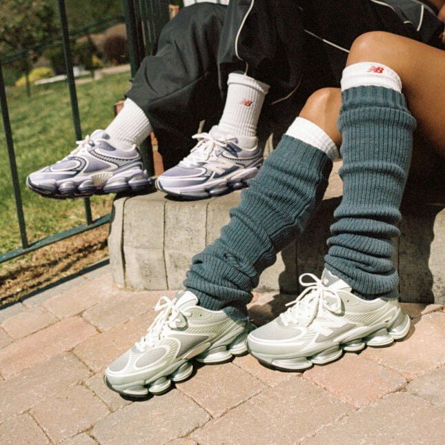 Two people sitting on a sidewalk wearing New Balance sneakers.