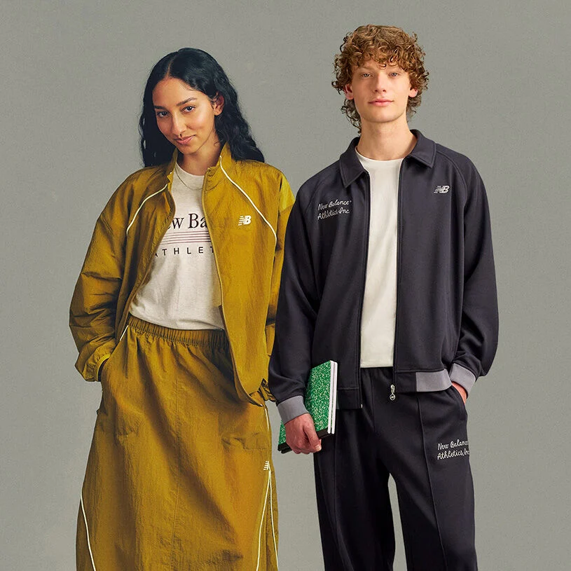Two people stand side by side against a plain light gray studio background in a clean, minimal composition with ample empty space below.