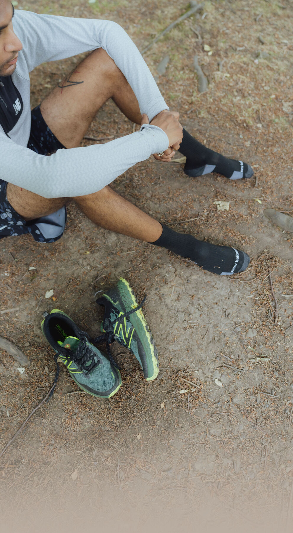 Man sitting on the ground with a pair of Fresh Foam X Hierro v7 beside him 