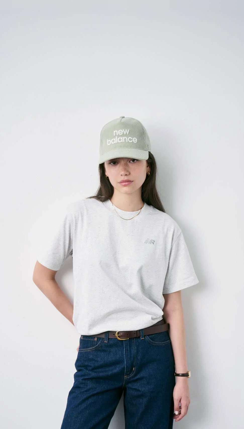 Mujer con gorra New Balance de pie frente a una pared blanca