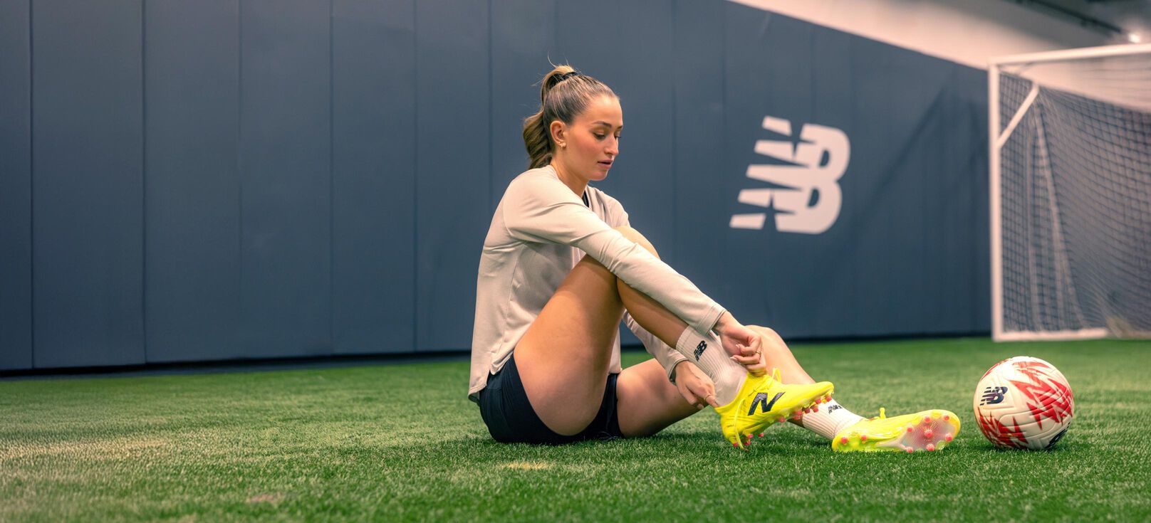 Jordyn Huitema sitting on the turf while tying her soccer cleats.  