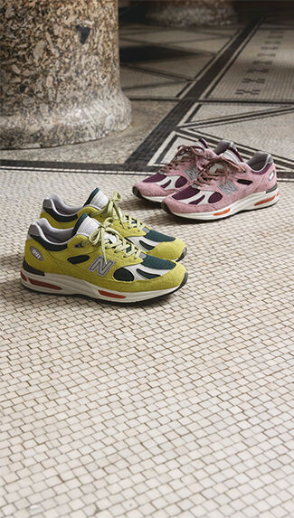 Two pairs of New Balance Made in UK sneakers on a textured white tiled floor.  
