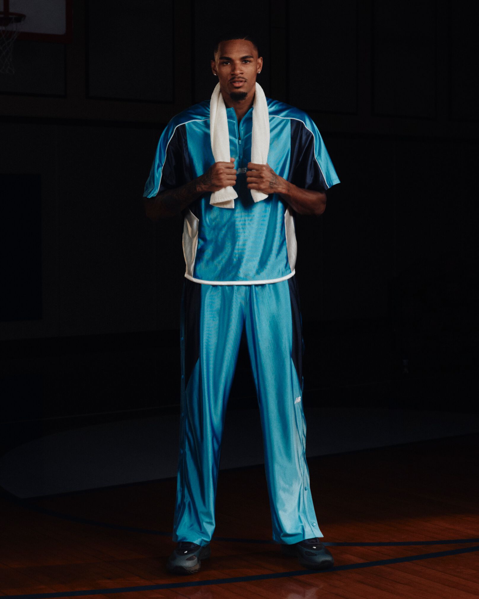 Person wearing a bright blue New Balance warm-up outfit with a white towel draped around the neck on an indoor basketball court.