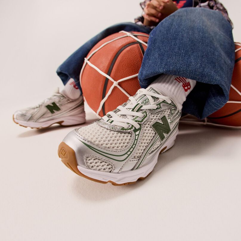 A kid wearing silver shoes sitting on a net of basketballs. 