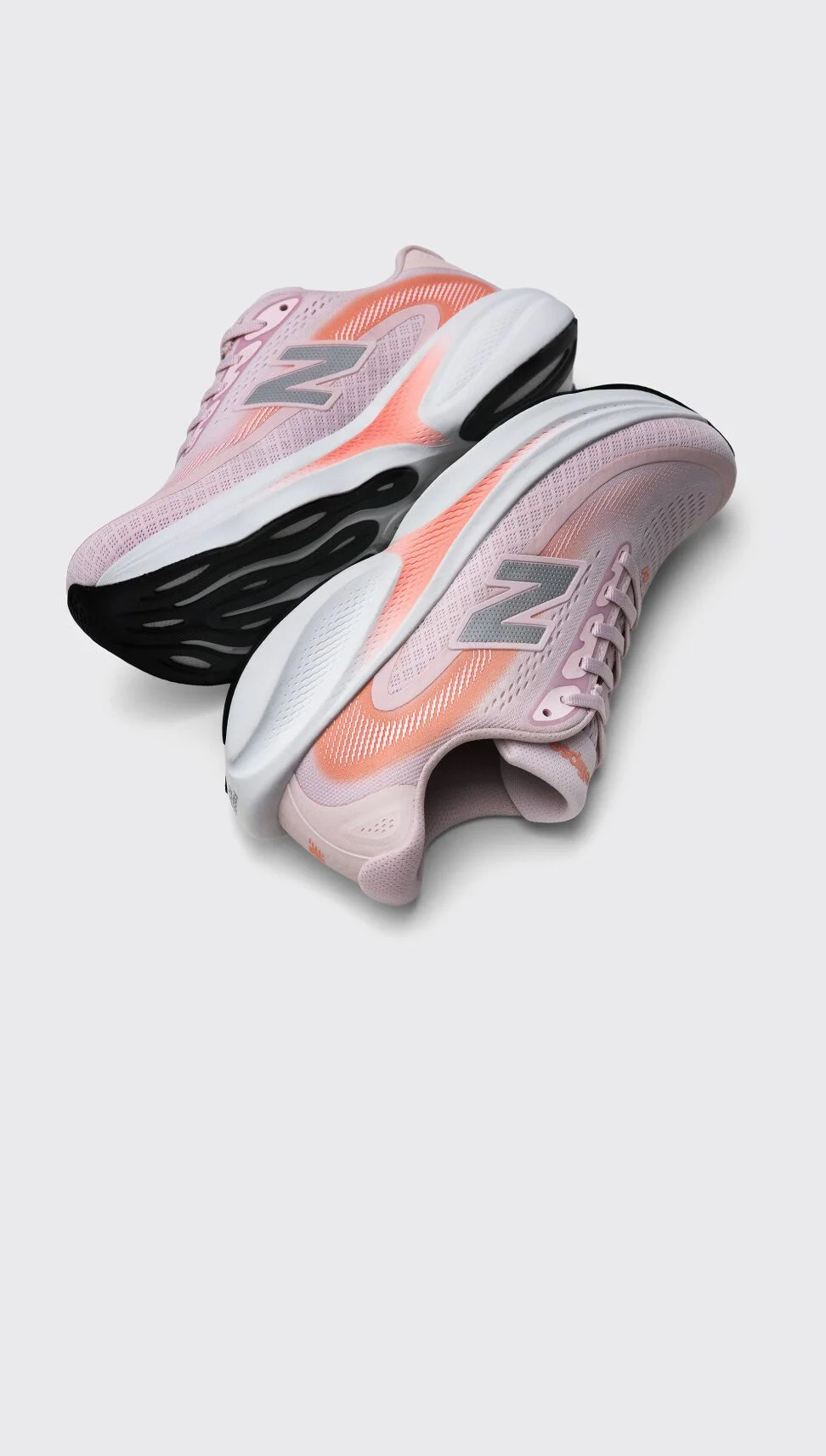 Pair of light pink New Balance running shoes with coral accents and chunky black-and-white soles displayed on a light gray background. 