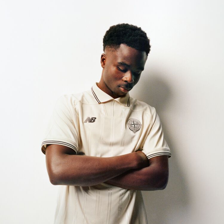 Saka looking down with his arms folded wearing a beige jersey.