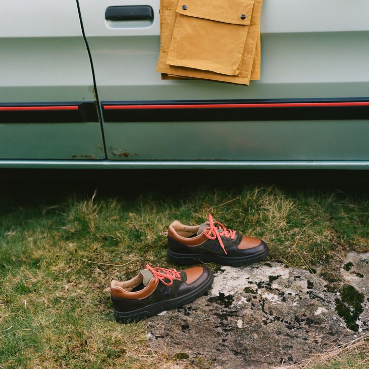 A pair of Drakes’s x New Balance shoes on the grass next to a vintage car.