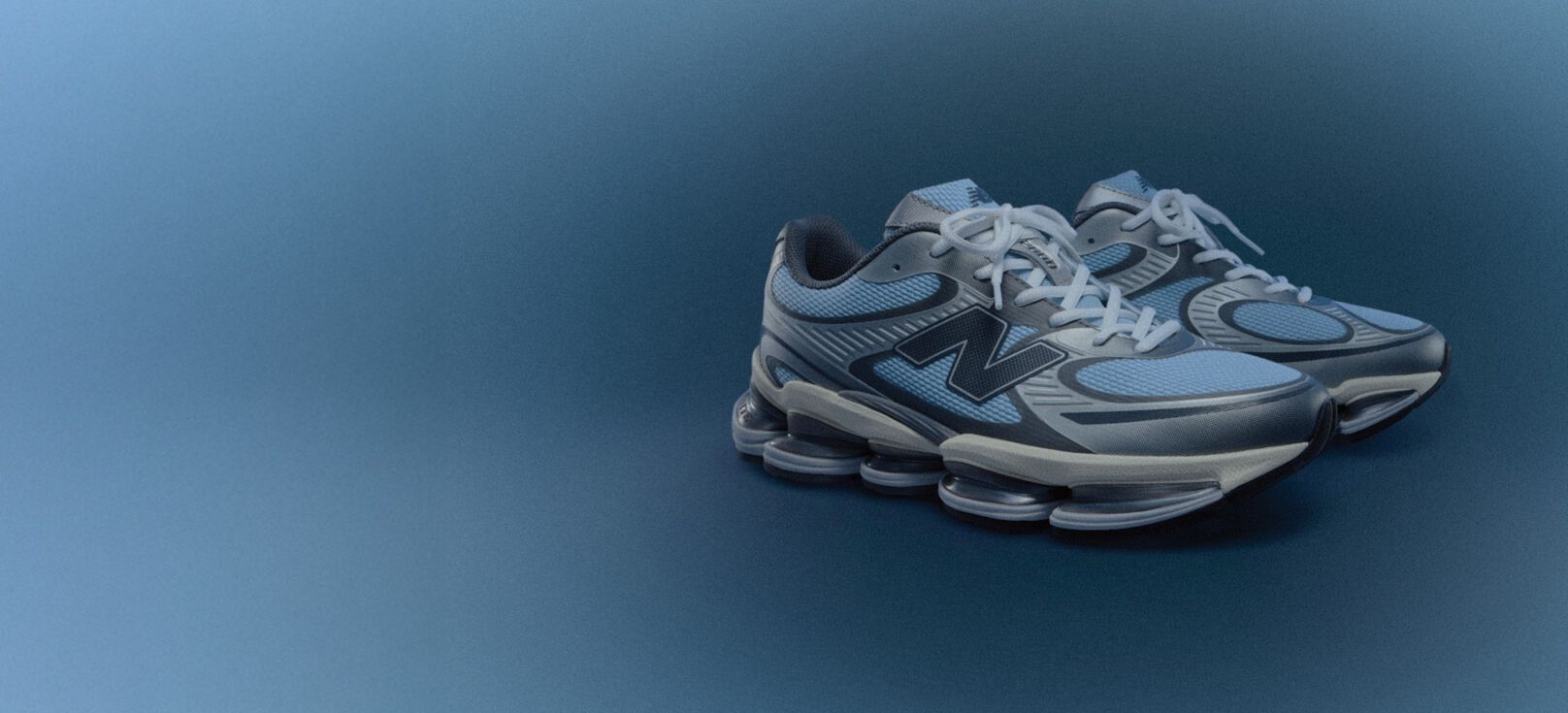 The ABZORB 2000 New Balance sneaker in an angled profile in light chrome blue and silver metallic over a blue radial gradient background. 