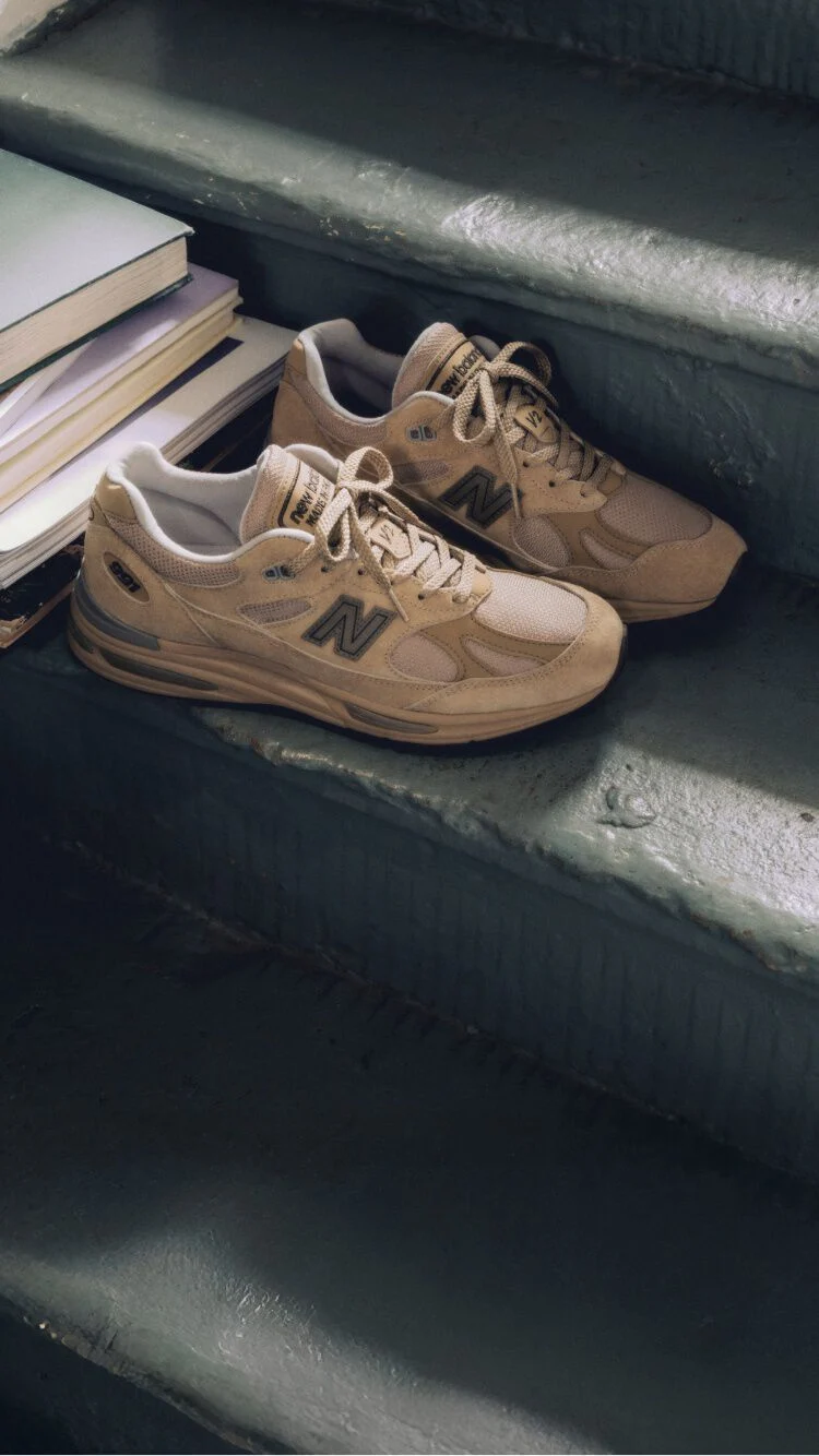Un par de tenis Made in UK de New Balance en una escalera, junto a una pila de libros.&nbsp;